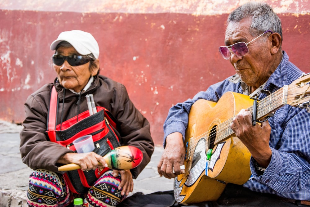 man in black and red jacket playing acoustic guitar