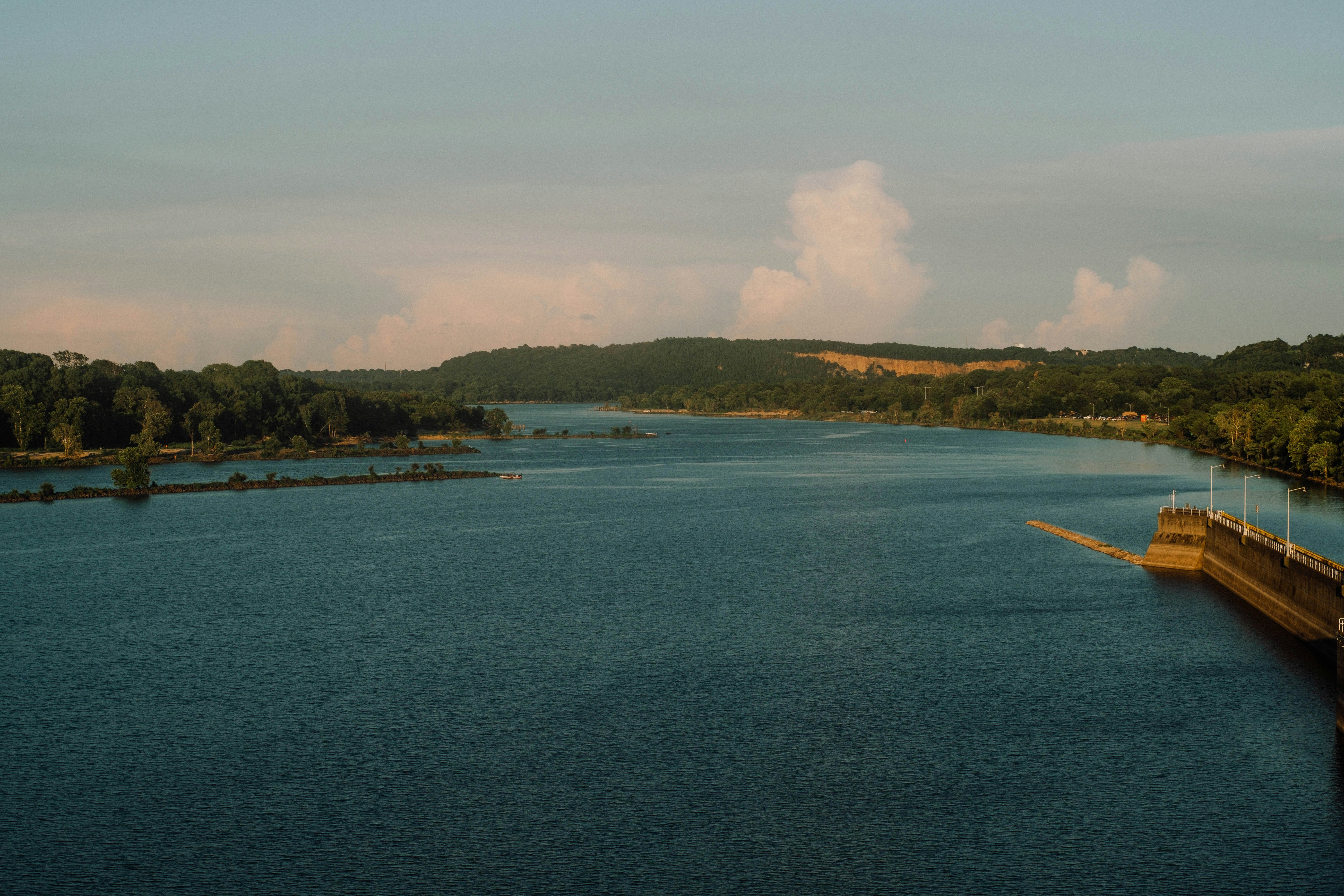 body of water near green trees under white clouds during daytime