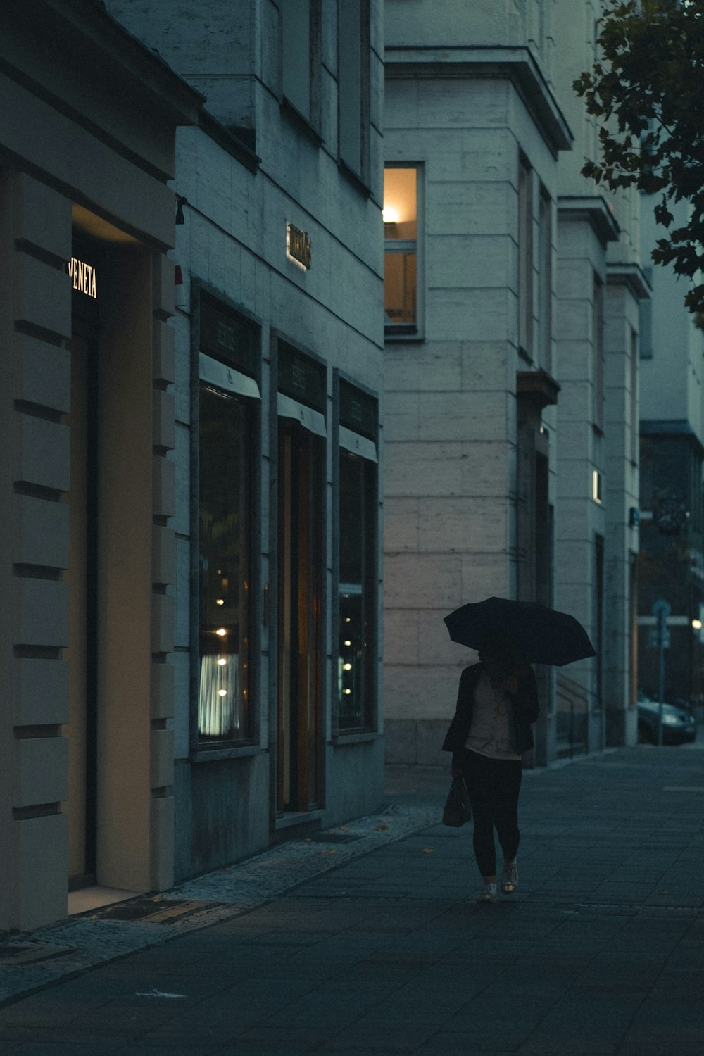 Person im schwarzen Mantel mit Regenschirm, die tagsüber auf dem Bürgersteig geht