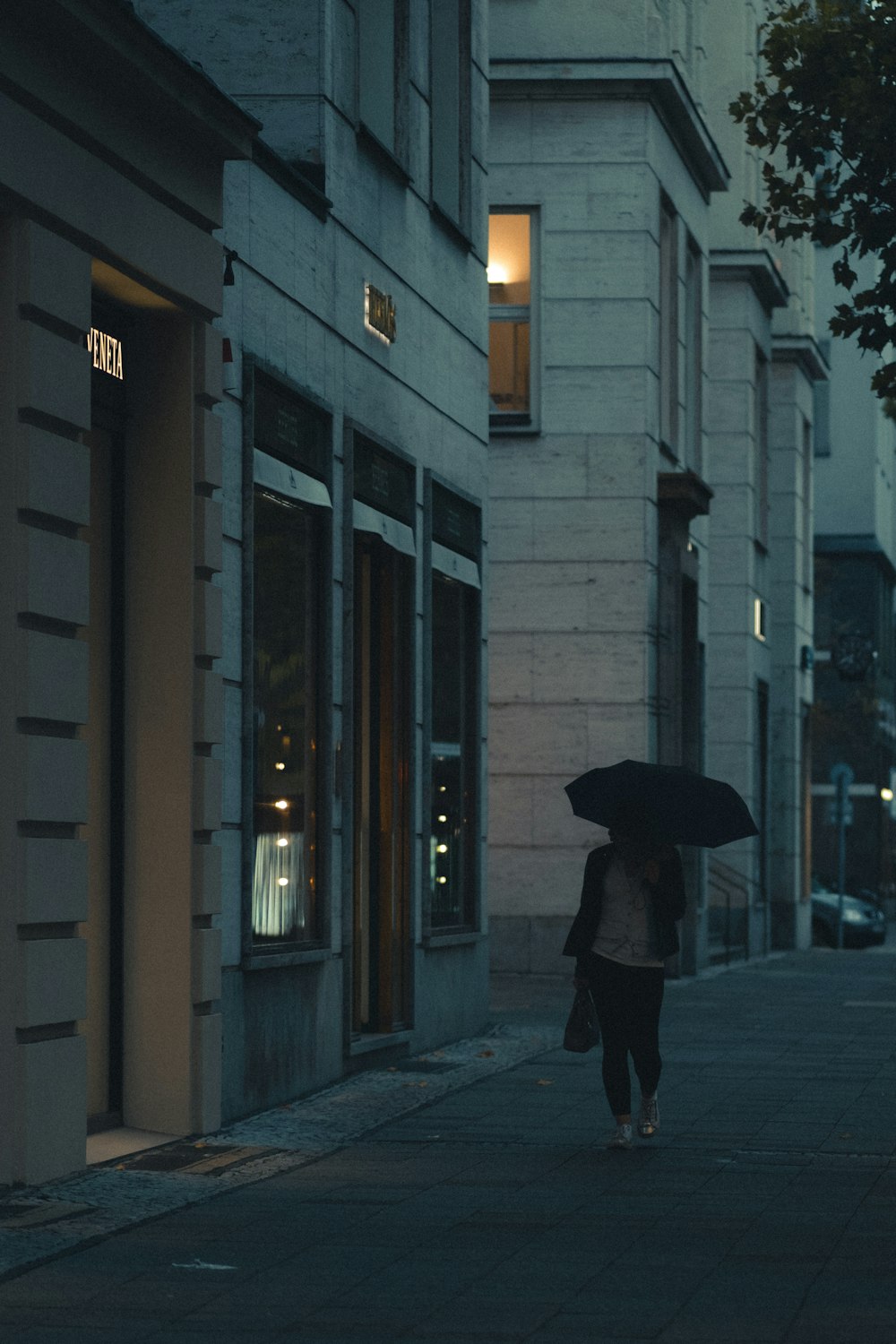 Personne en manteau noir tenant un parapluie marchant sur le trottoir pendant la journée
