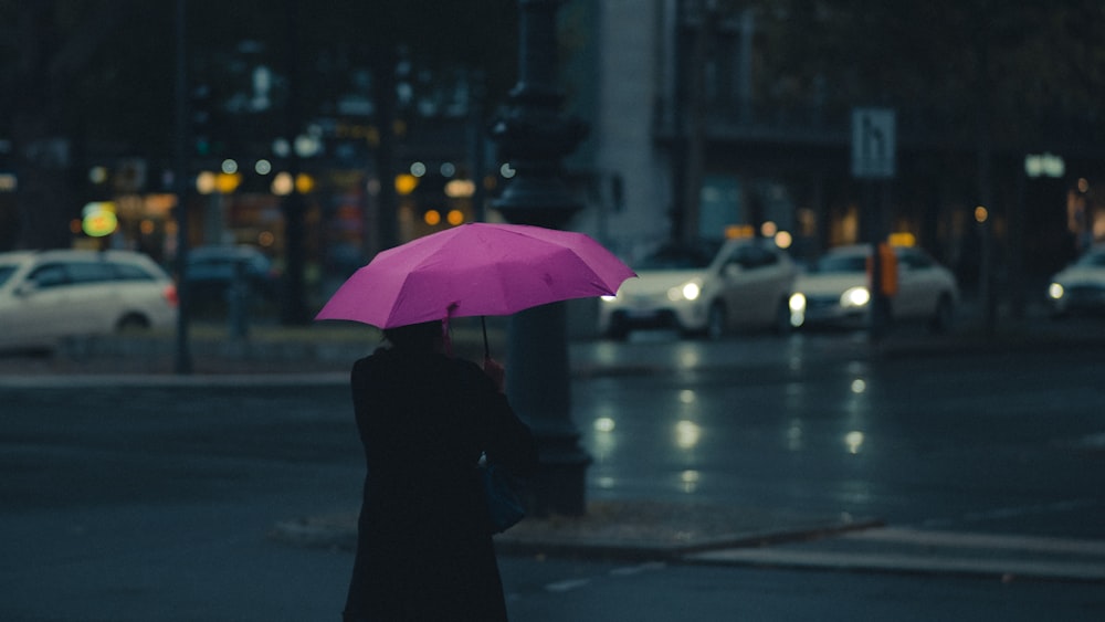 personne en manteau noir tenant un parapluie rose