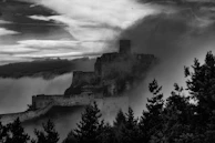 A shadowy medieval castle perched on a misty hill at dawn.