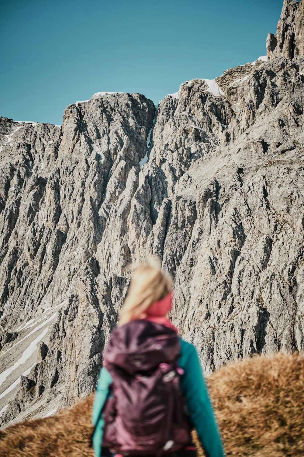 woman in purple jacket standing near rocky mountain during daytime
