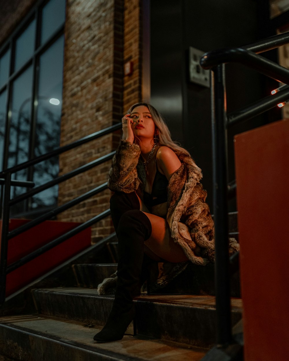 woman in black pants and brown jacket sitting on black metal staircase