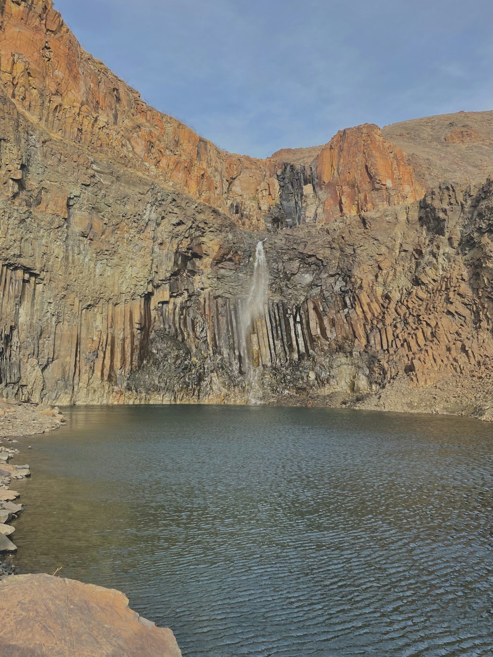 brown rocky mountain beside body of water during daytime