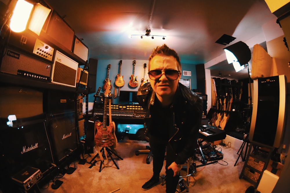 man in black leather jacket standing beside black and brown electric guitar