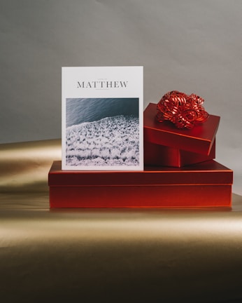 A card with a textured design sits upright against a backdrop of vibrant red gift boxes. A decorative ribbon accents the top box. The card features an ocean wave pattern across the lower section.