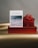 A card with a textured design sits upright against a backdrop of vibrant red gift boxes. A decorative ribbon accents the top box. The card features an ocean wave pattern across the lower section.