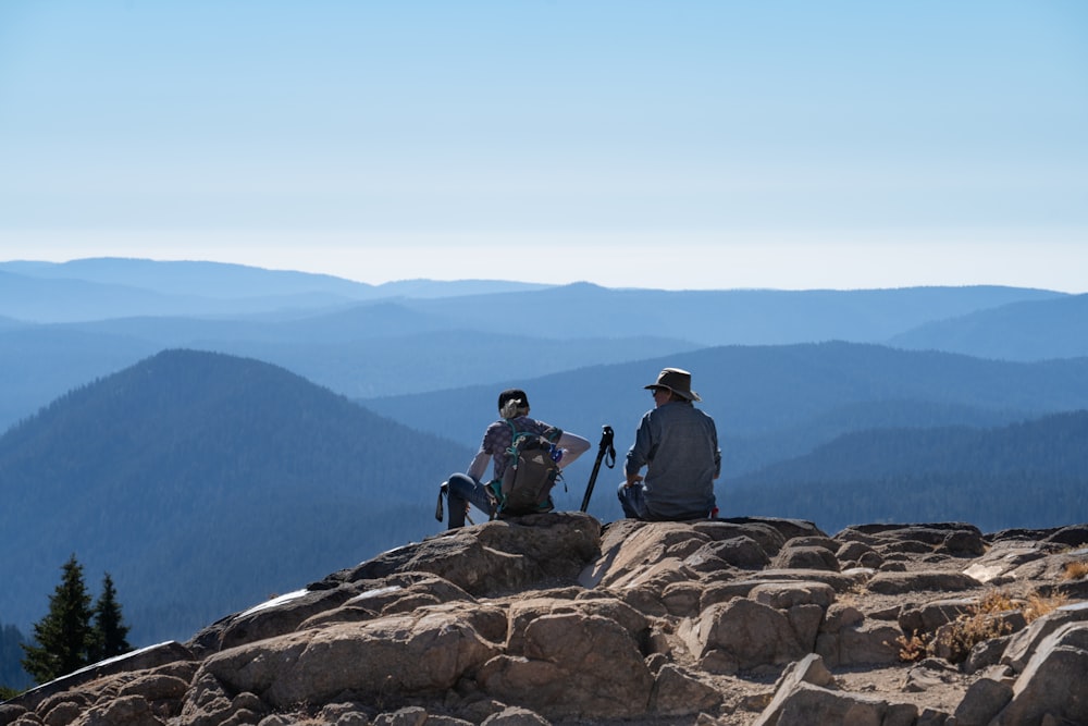 3 hommes assis sur une formation rocheuse brune pendant la journée