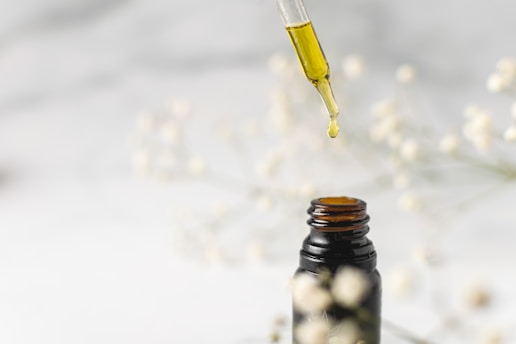 Aromatic essential oil drops falling into a glass container with fresh herbs nearby