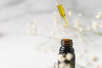 A close-up of a dropper releasing golden hair growth oil onto healthy, shiny hair strands.