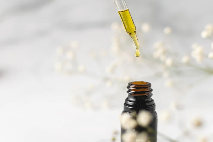 Close-up of a dropper releasing essential oil onto fresh green leaves.