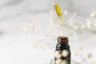 Close-up of a glass dropper releasing golden facial oil, set against a soft sage green background.