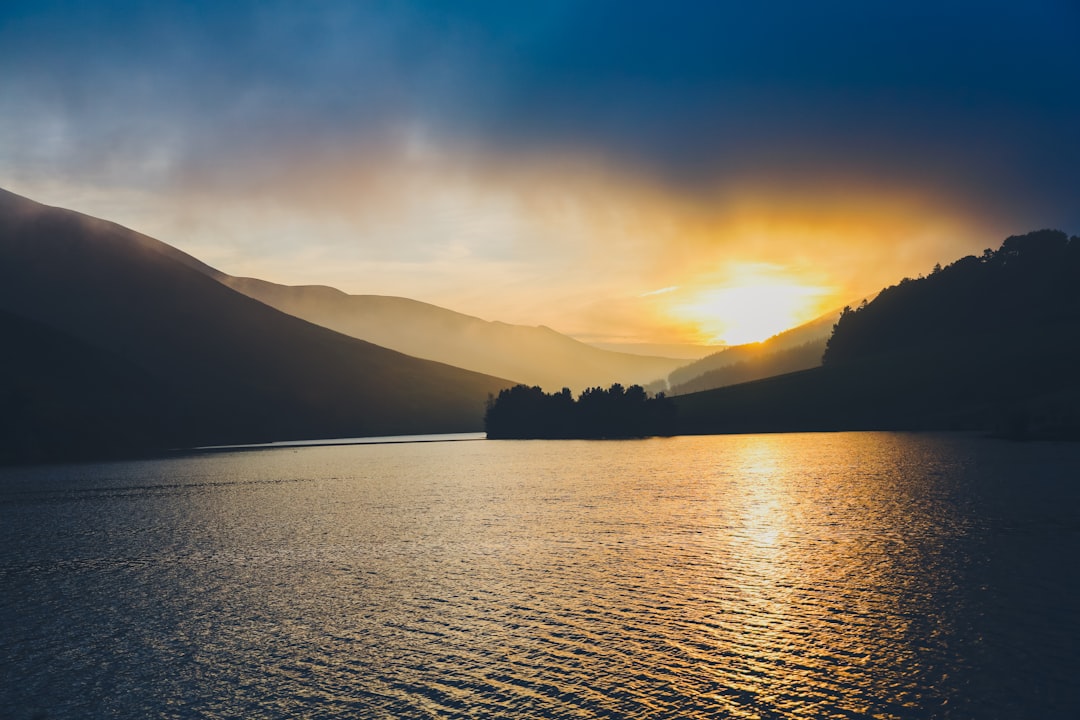 silhouette of mountain near body of water during sunset