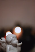 A delicate angel figurine beside a glowing candle on a minimalist wooden table