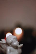 A delicate angel figurine beside a glowing candle on a minimalist wooden table