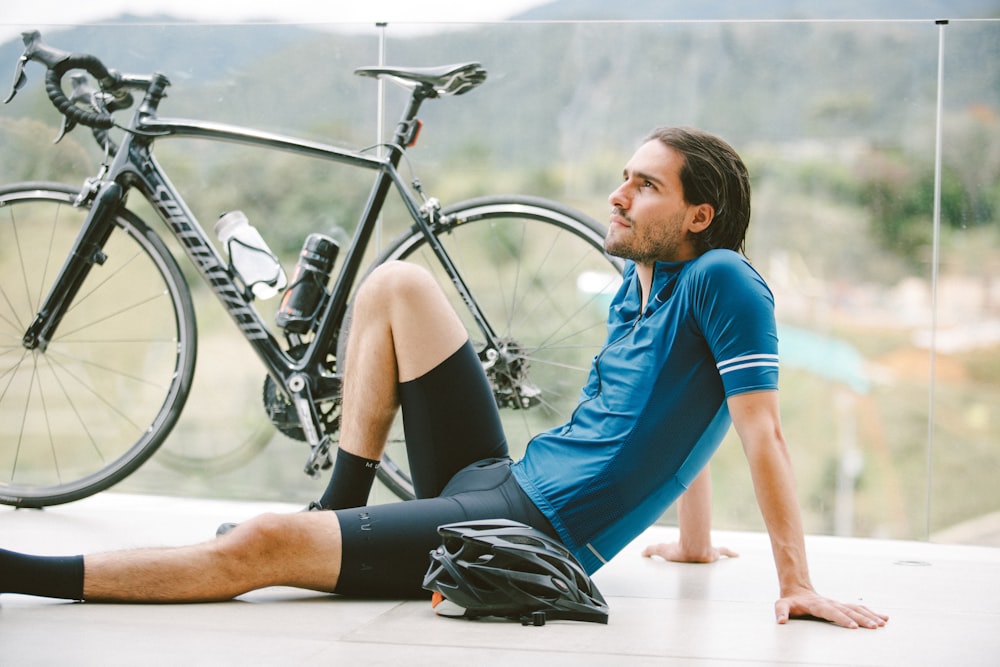 woman in blue shirt and black shorts sitting on floor beside black road bike