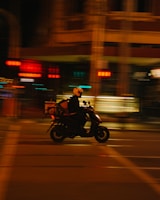 A friendly courier on a motorcycle navigating city streets with a package.