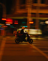 Delivery rider on a motorcycle speeding through city streets at night.