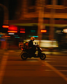 Delivery rider on a motorcycle speeding through city streets at night.