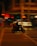 A motorcyclist, wearing a helmet and carrying a delivery box, rides swiftly on a scooter through a dimly lit urban street. The background is blurred, emphasizing the motion and speed of the motorbike.