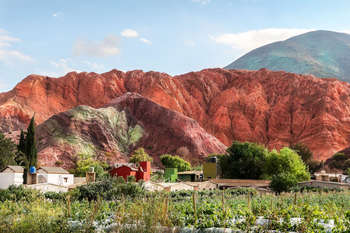 Red and green-streaked hills above houses and a planted field in Purmamarca