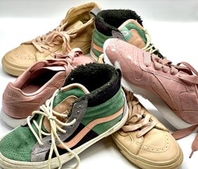 A collection of sneakers in various styles and colors displayed together, featuring textures like faux reptile skin and suede. The sneakers include high-top and low-top designs with detailed stitching and laces.