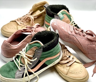 A collection of sneakers in various styles and colors displayed together, featuring textures like faux reptile skin and suede. The sneakers include high-top and low-top designs with detailed stitching and laces.