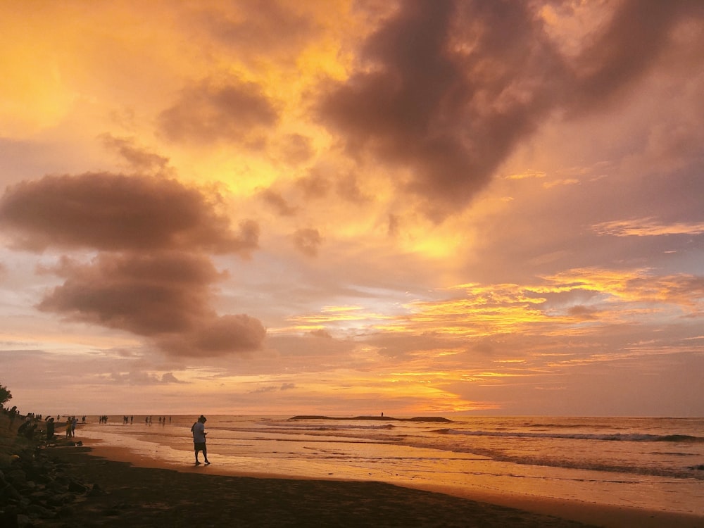 silhouette of person standing on seashore during sunset