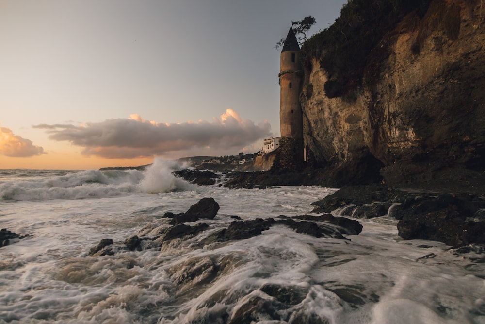 brown concrete building on top of rocky hill by the sea during sunset