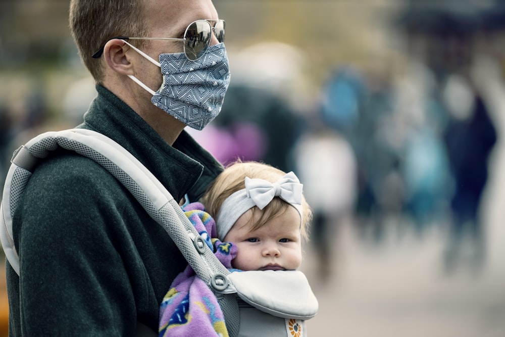 man in black jacket carrying baby in white and purple shirt