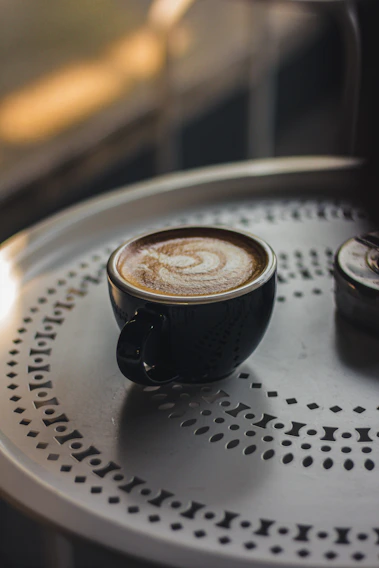 A beautifully arranged latte art in a sleek black cup on a dark wooden table with soft ambient lighting.
