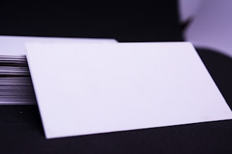 A stack of blank, white cards is placed on a dark surface with one card prominently displayed on top, slightly tilted to the side.