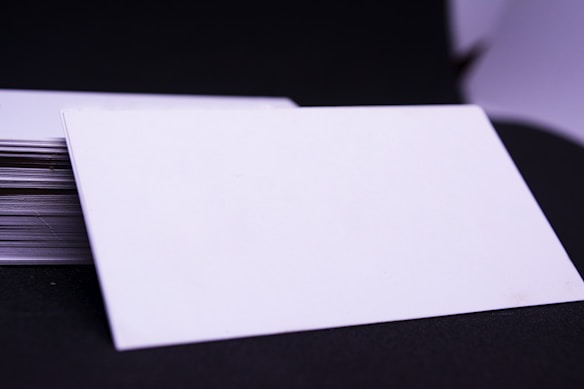 A stack of blank, white cards is placed on a dark surface with one card prominently displayed on top, slightly tilted to the side.