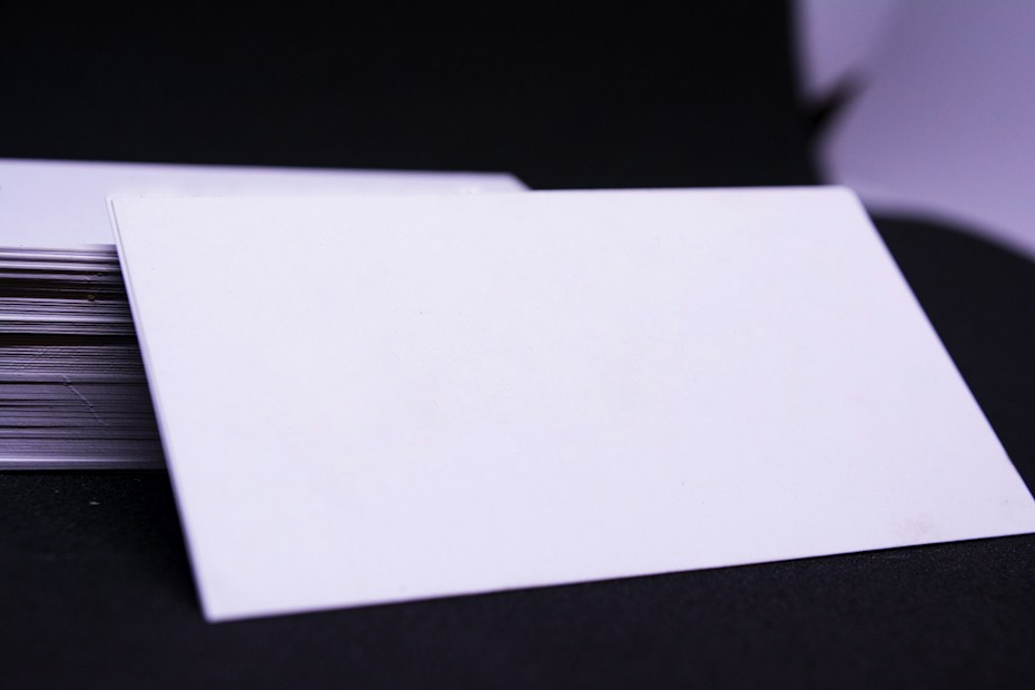 A stack of blank, white cards is placed on a dark surface with one card prominently displayed on top, slightly tilted to the side.
