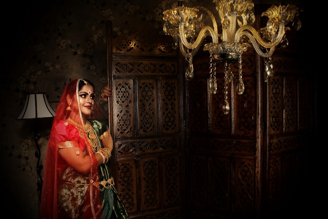 woman in red and brown sari standing beside brown wooden door