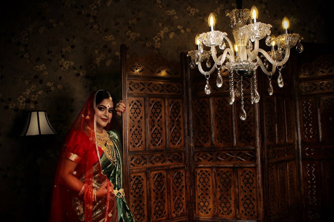 woman in red and green sari standing beside brown wooden door