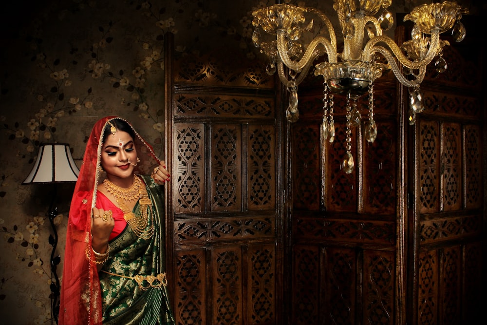 Mujer con hiyab floral rojo y verde de pie junto a la puerta de madera marrón