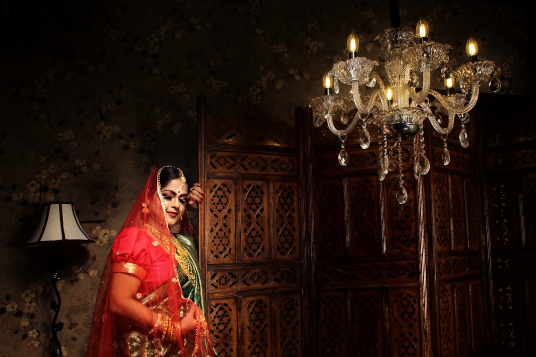 woman in red and green sari standing beside brown wooden cabinet