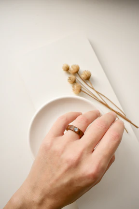 Hand wearing a delicate resin ring featuring a small, suspended flower inside.
