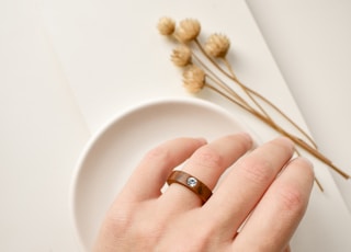 person wearing gold wedding band holding white ceramic plate
