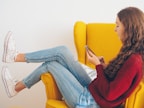 woman in red sweater and blue denim jeans sitting on yellow couch