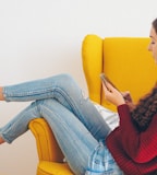 woman in red sweater and blue denim jeans sitting on yellow couch