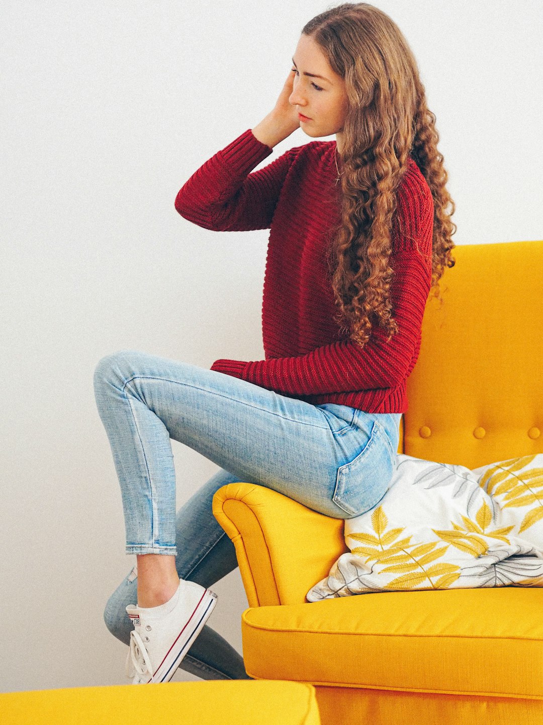 woman in red sweater and blue denim jeans sitting on yellow sofa