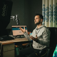 man in gray sweater sitting on chair in front of laptop computer