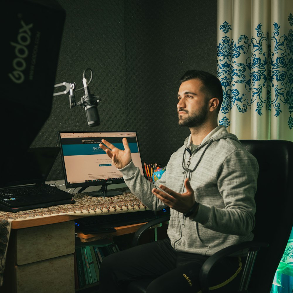 man in gray sweater sitting on chair in front of laptop computer