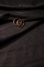 A delicate close-up of intertwined wedding rings resting on soft beige fabric with gentle golden light.