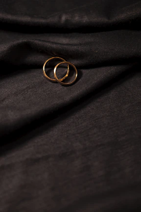 Close-up of delicate wedding rings resting on dark velvet fabric, highlighting intricate details.