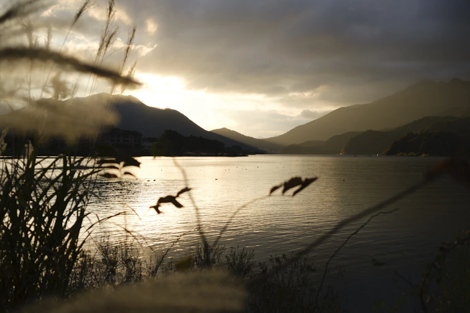 Serene lake surrounded by mountains with hazy sunset casting orange glow over landscape