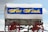 A classic covered wagon with a white canvas top and blue and yellow text reading 'West Winds.' The wagon has red wheels and a wooden structure underneath the canvas. The wagon is set against a partly cloudy sky.